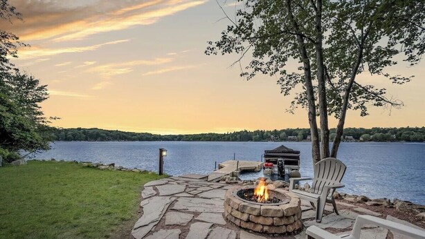 A stone fire pit with a fire, two Adirondack chairs, and a view of a lake at sunset. - Water's Edge!  11 Bdrm, 5.5 Bath, Lakefront, Dock, Sleeps 35, Hot Tub, IR Sauna (Lake Harmony)