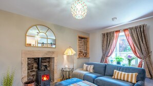 A cozy living room with a stone fireplace, a blue sofa, a striped throw, and a hanging light fixture. - Cooriedoon by Interhome (Hopeman)