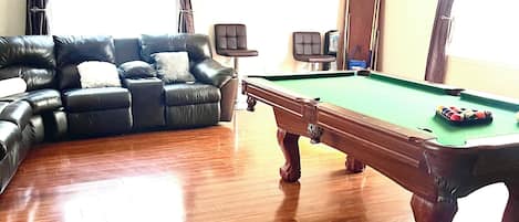 A living room with a pool table, a leather sofa, and a ceiling fan.