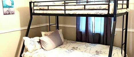 Un lit superposé dans une chambre dotée d’un ventilateur de plafond, d’une fenêtre avec des rideaux et d’un sol recouvert de moquette.