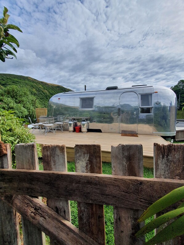 Un camper argentato con zona cucina, comprensiva di fornello e lavandino, circondato da un patio in legno e una recinzione di legno.