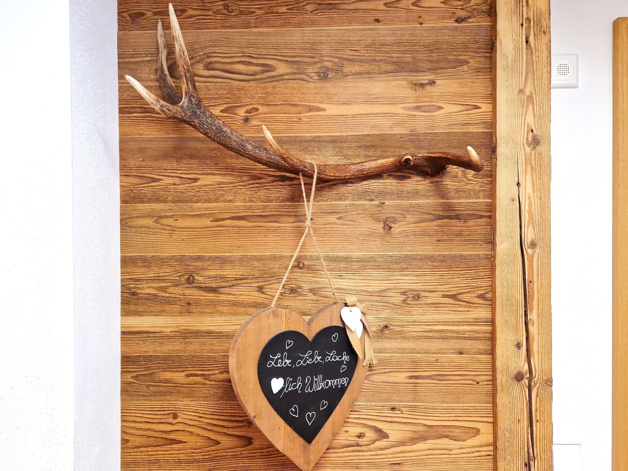 Una rama de madera con una pizarra en forma de corazón que muestra un mensaje en alemán.