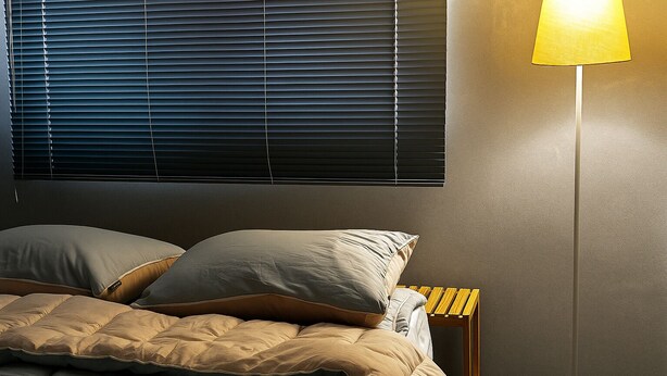 Un dormitorio con cama, almohadas, una mesita de noche y una lámpara de pie.