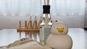 Una mesa con una botella de perfume, un muñeco de nieve decorativo y una pequeña bolsa con texto.