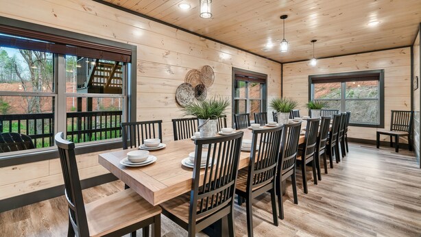 Une salle à manger aux murs lambrés, avec une longue table dressée pour six personnes, entourée de chaises.