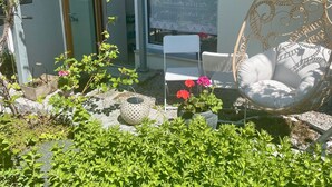 Ein Balkon mit Korbstuhl, weißem Stuhl und einer Topfpflanze.