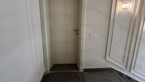 A narrow hallway with a closed door at the end, a light switch on the wall, and a carpeted floor.