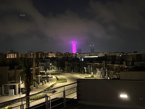 Vue nocturne d’un quartier résidentiel avec des immeubles, une route sinueuse et une tour illuminée en rose au loin.
