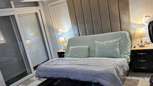 A bedroom with a bed, a nightstand, a lamp, a drawer unit, and a sliding door.