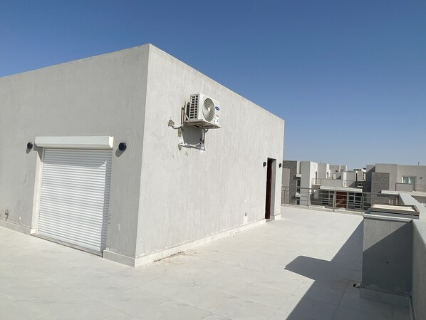 A modern building with a closed shutter, an air conditioning unit, and a clear sky.