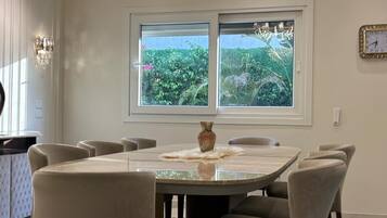 A dining area with a table and chairs, a vase, and a window with a view of greenery.