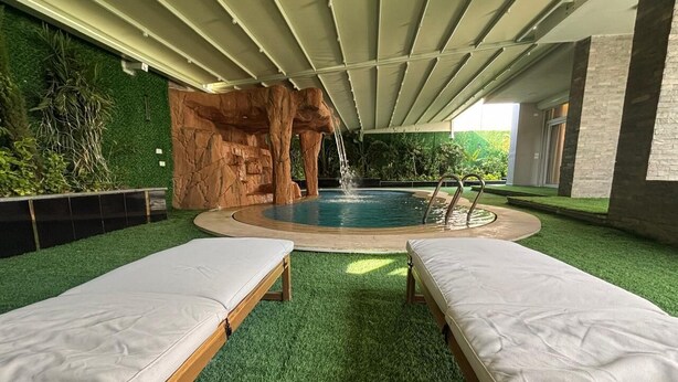 A spa area with two lounge beds, a hot tub, and a rock wall.