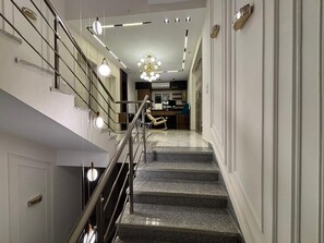 Una escalera moderna con barandilla de metal que conduce a un espacio bien iluminado con un candelabro.