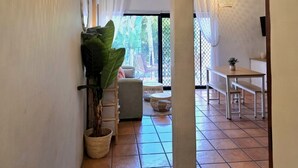 Un couloir orné d’un luminaire suspendu en fibres tressées, d’une plante en pot et offrant une vue sur un coin repas avec une table et des chaises.