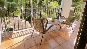 Un balcon agrémenté de chaises et d’une table en osier, entouré d’une balustrade et de plantes en pot.