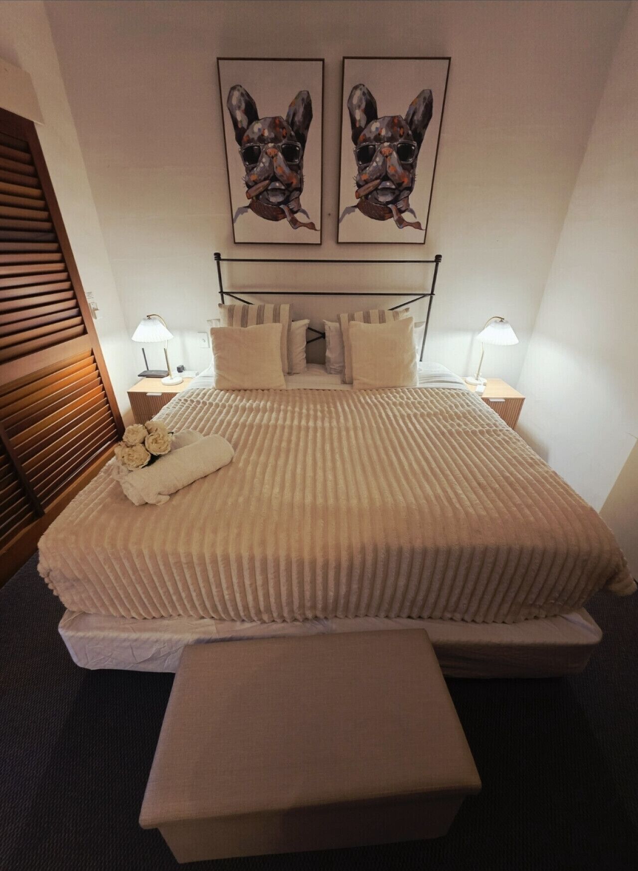 Una cama bien hecha con una manta texturizada, dos lámparas de noche, un cabecero de madera y dos cuadros en la pared.