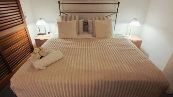 Una cama bien hecha con una manta texturizada, dos lámparas de noche, un cabecero de madera y dos cuadros en la pared.