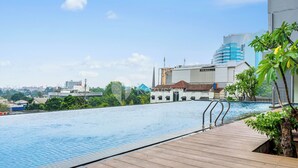 A rooftop swimming pool with a wooden deck, surrounded by buildings and greenery. - Suvin by Kozystay - Pondok Indah (Jakarta)