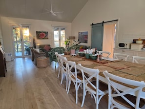 A dining area with a table set for four, surrounded by white chairs, a ceiling fan, and a view of the outdoors through large windows. - Unwind at new and beautiful Blue Wren Hill (Gloucester)