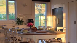 Un comedor con una mesa de madera, sillas blancas y vistas a través de las ventanas.