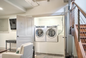 A laundry room with two front-loading washing machines, a small table, and a chair.