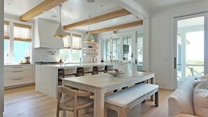 Une cuisine spacieuse dotée d’un grand îlot central, de poutres en bois et offrant une vue sur l’extérieur.