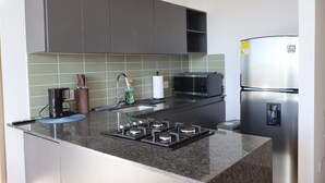 A modern kitchen with grey cabinets, a stainless steel refrigerator, a microwave, a gas stove, and a coffee maker. - Asturias apartment for family or business (CERRITOS)