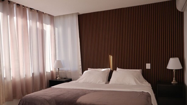 A hotel room with a bed, two bedside tables, a window with curtains, and a wooden wall panel. - Asturias apartment for family or business (CERRITOS)