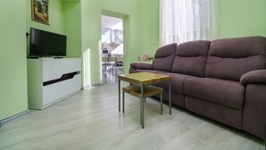 Una sala de estar con un sofá, un televisor sobre un mueble, una mesita y vistas al exterior.