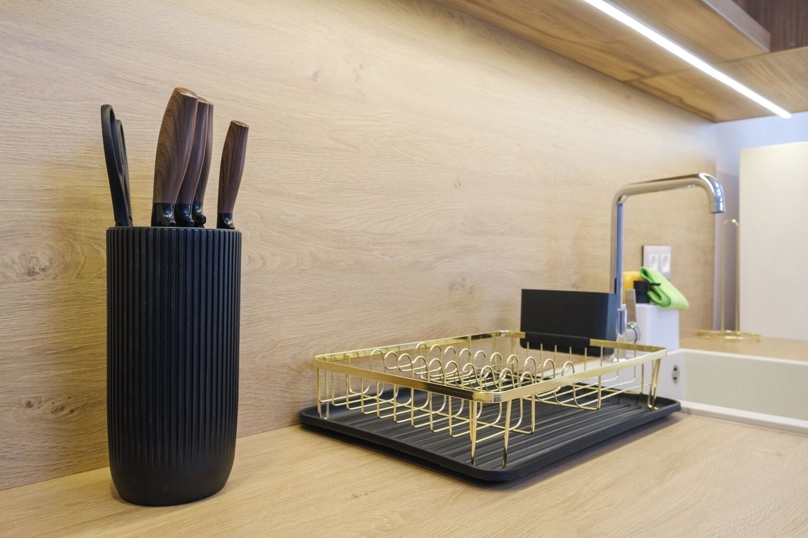 A kitchen with a black ribbed container holding knives, a gold wire fruit basket, and a modern faucet.