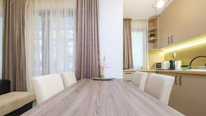 A modern dining area with a wooden table, white chairs, and a vase with dried plants. - Comfort 1 Bedroom App (Plovdiv)