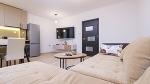 A modern living room with a sofa, a small round table, and a TV mounted on the wall. - Comfort 1 Bedroom App (Plovdiv)