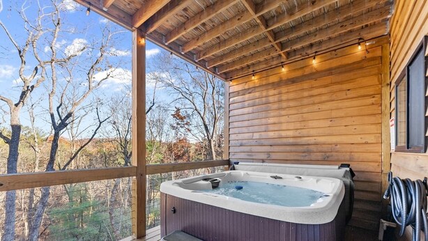 A wooden cabin with a hot tub and a deck overlooking a forest.