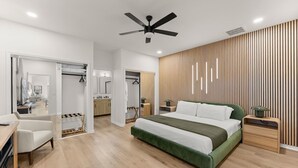 A modern bedroom with a large bed, a ceiling fan, a wooden panel wall, and a walk-in closet.