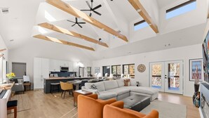 A spacious living area with a large sectional sofa, orange armchairs, and a kitchen in the background.