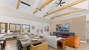 A spacious living area with a large wooden dining table, a fireplace, and a television mounted on a wooden wall.