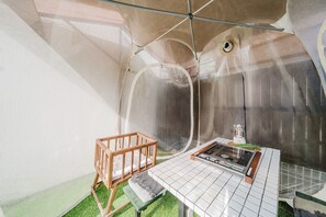 Une chambre de taille modeste, équipée d’un lit bébé, d’une table avec une bouilloire et d’un petit radiateur.