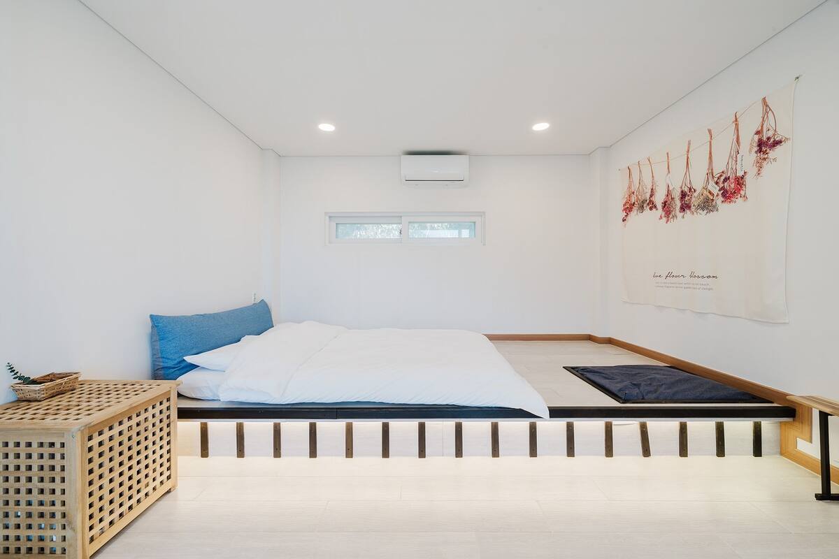 Une chambre à coucher minimaliste, avec un lit, une petite table et un climatiseur fixé au mur.
