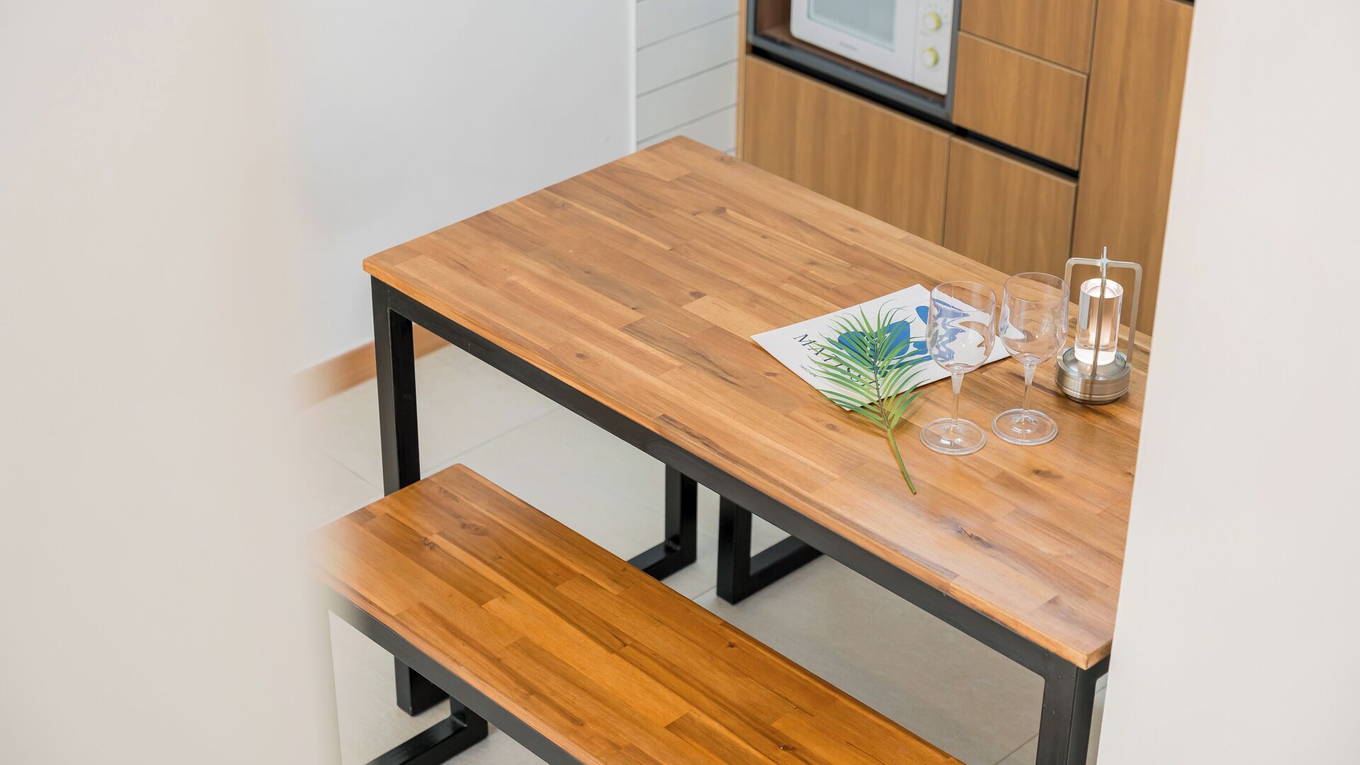 A wooden table with a bench, a menu, and a candle holder in a modern kitchen setting.