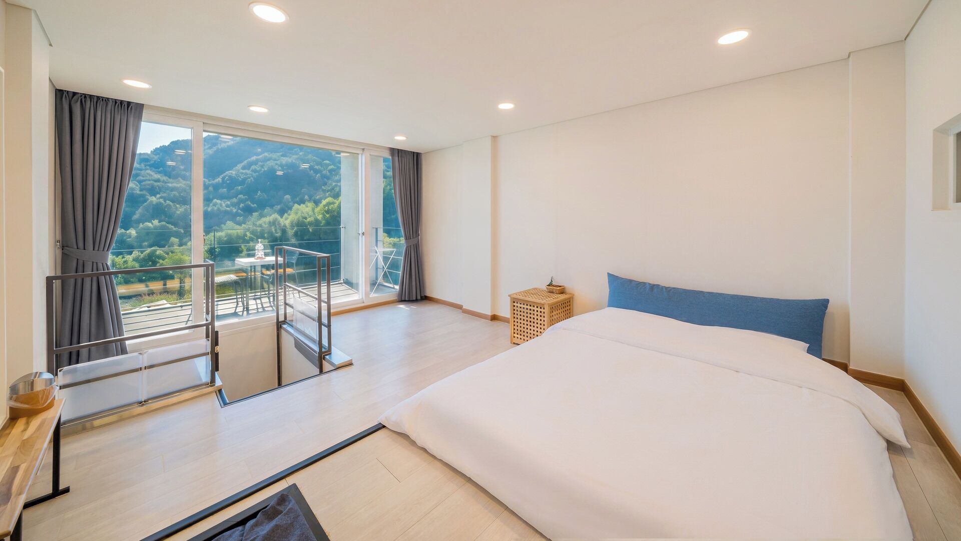 A hotel room with a large bed, a balcony with a view of the mountains, and a small table with chairs.