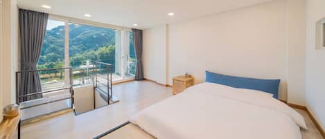 A hotel room with a large bed, a balcony with a view of the mountains, and a small table with chairs.