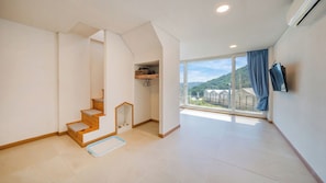 Ein geräumiger Raum mit einer Holztreppe, einem großen Fenster mit Blick ins Grüne und einem angebrachten Fernseher.