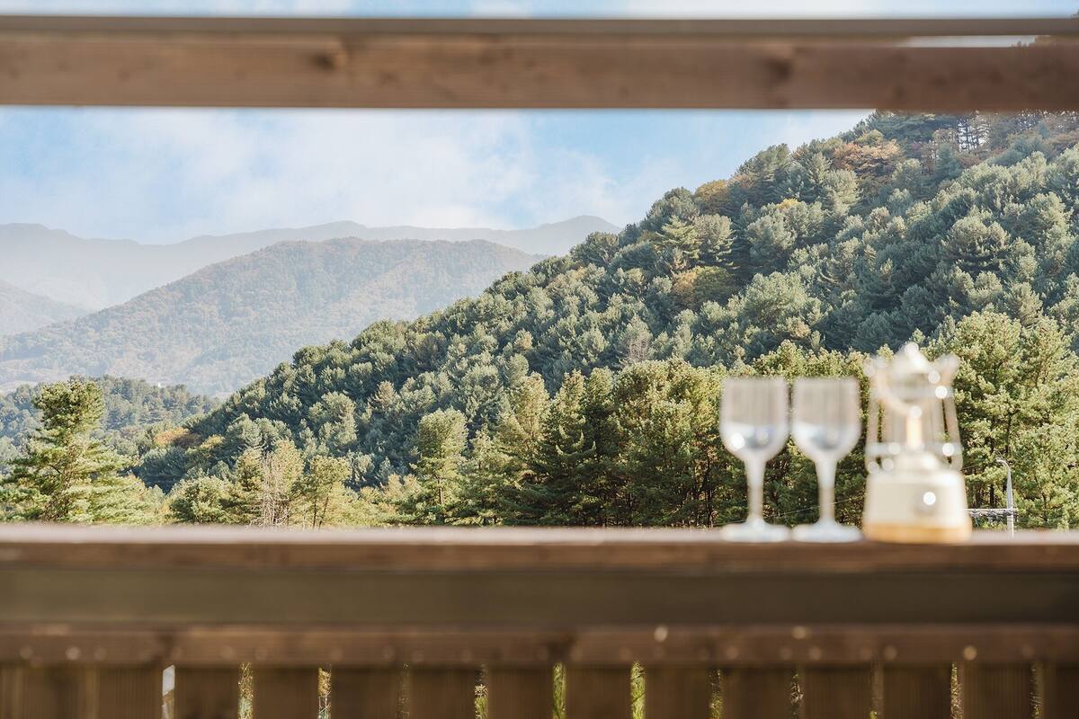 Une vue sur un paysage montagneux avec une terrasse en bois et deux verres posés dessus.