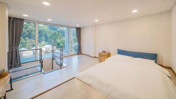 A bedroom with a large bed, a balcony with a railing, and a view of greenery outside.
