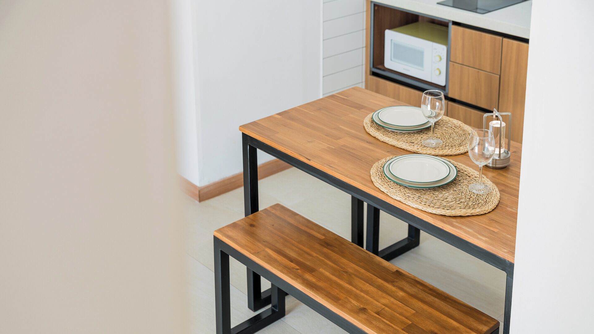 A wooden dining table with two placemats, a glass, and a candle holder.