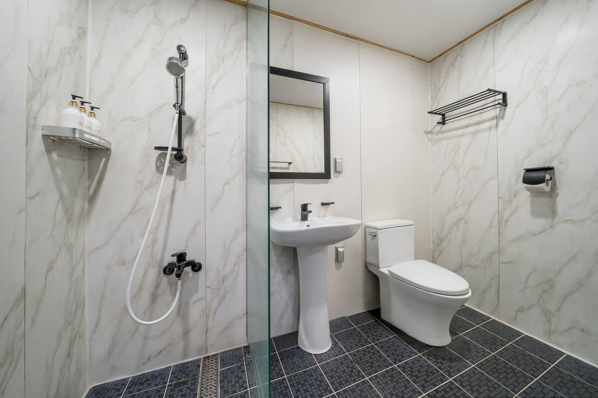 Un baño moderno con cabina de ducha de vidrio, un lavamanos pedestal blanco y un inodoro.