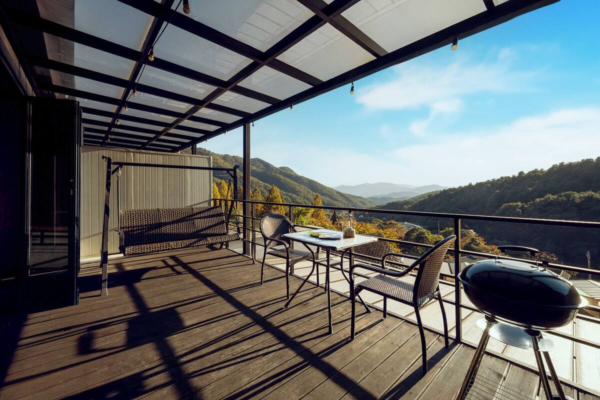 Un balcón con mesa, sillas y una parrilla, con vistas a un paisaje montañoso.
