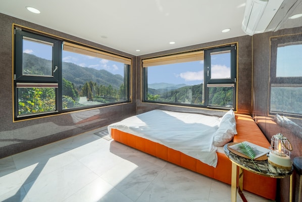 Camera da letto con un letto grande, un comodino e vista sulle montagne attraverso ampie finestre.