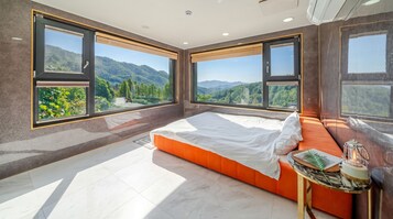 A bedroom with a bed, a nightstand, and a view of mountains.