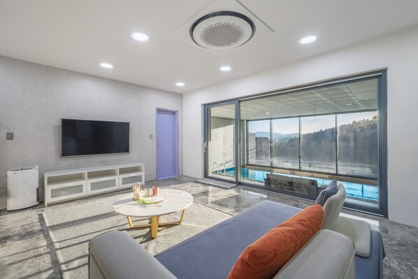 Una sala de estar moderna con un televisor de pantalla plana, un sofá, una mesa de centro y un amplio ventanal con vistas a una piscina.